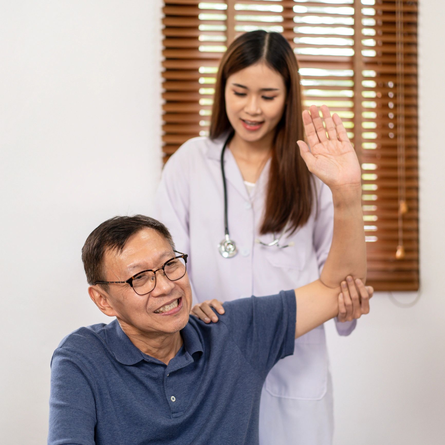 Healthcare professional assisting an older patient with arm exercises in a clinical setting